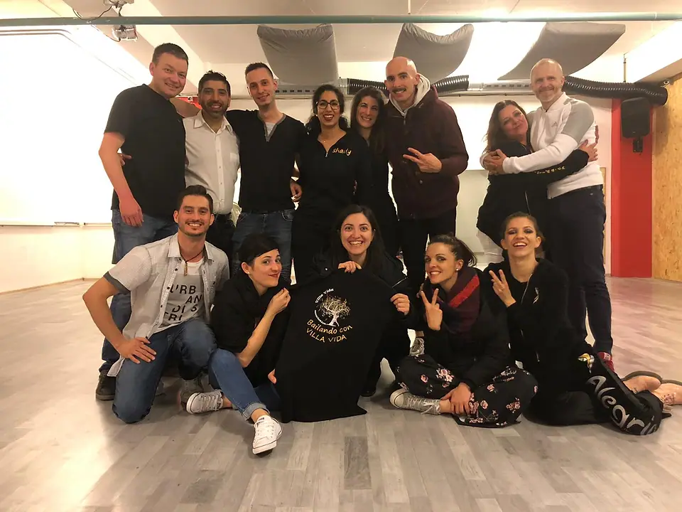 Un groupe d’amis dans une salle de danse, accroupis autour d’un t-shirt Bailando con Villa Vida.