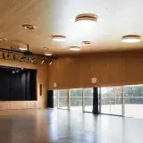 La grande salle des Utins à Echandens : parquet sombre, plafond en bois, scène aux rideaux noirs.